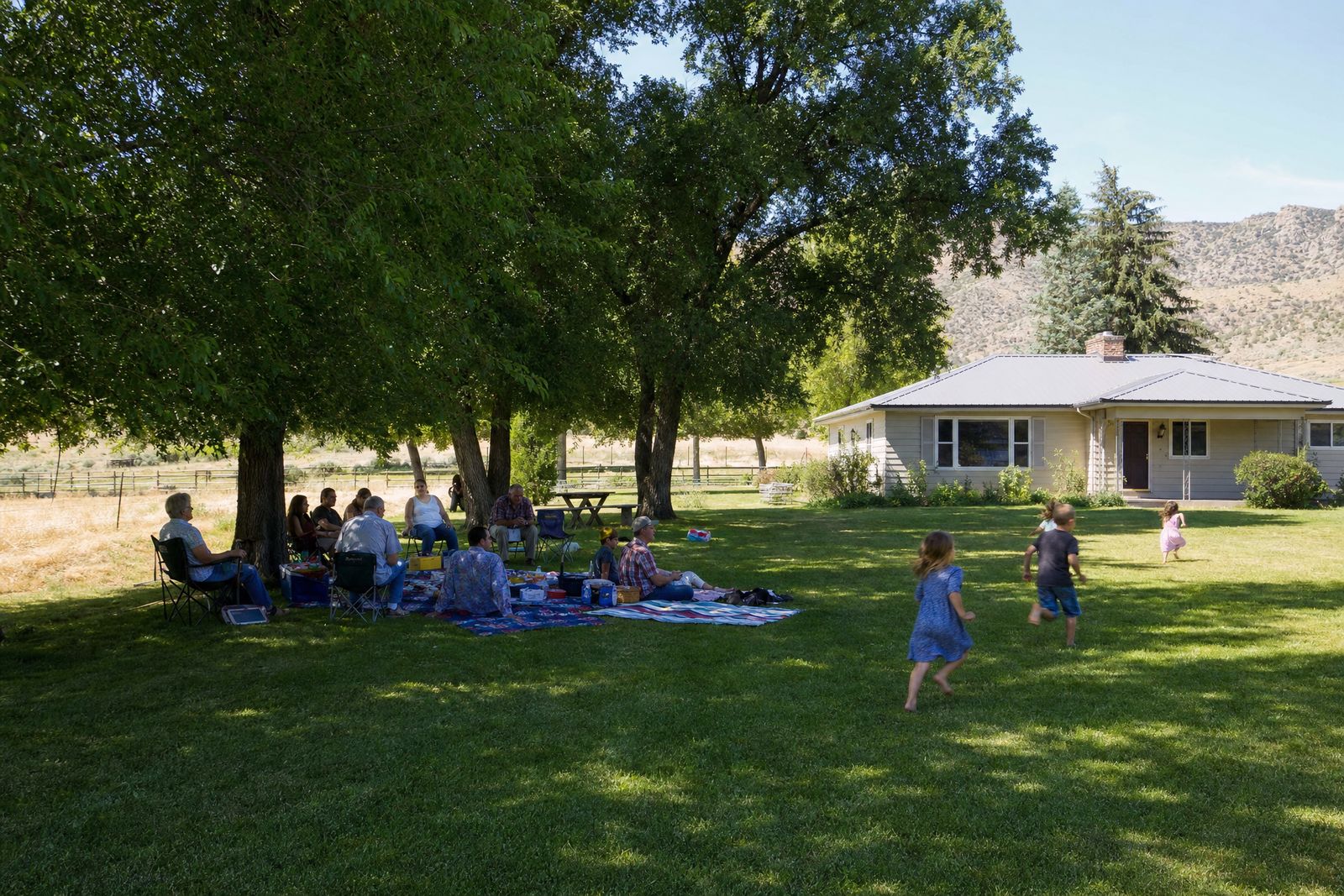 Family picnic under shade trees beside a ranch house