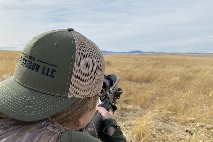Shooter behind a rifle scope in open grassland