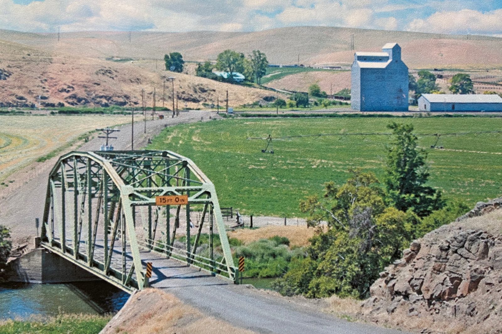 Truss bridge over the river, with hay ground and a grain elevator on the valley floor